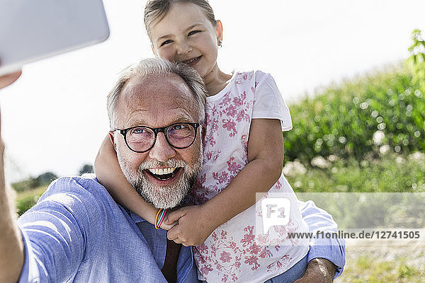 Mature man and little girl making fun selfies in the field