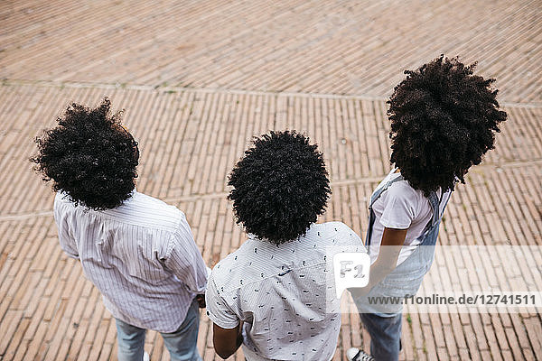 Back view of three friends with curly hair standing on a square