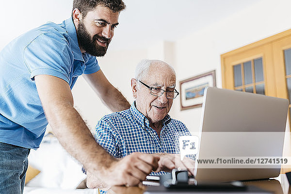 Adult grandson teaching his grandfather to use laptop