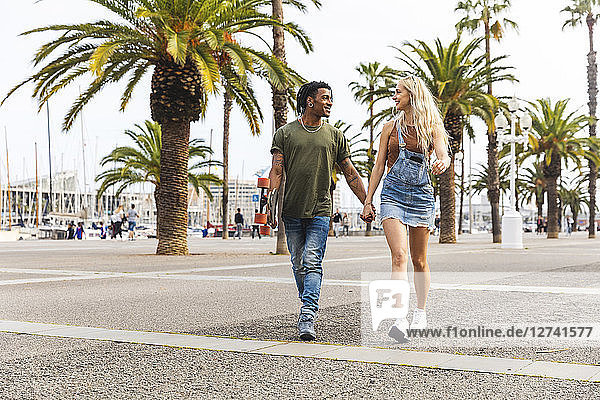 Spain  Barcelona  multicultural young couple walking hand in hand on promenade