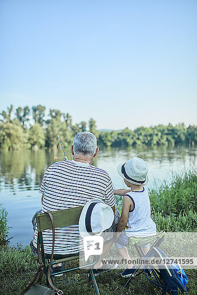 Back view of grandfather and grandson fishing togetehr at lakeshore