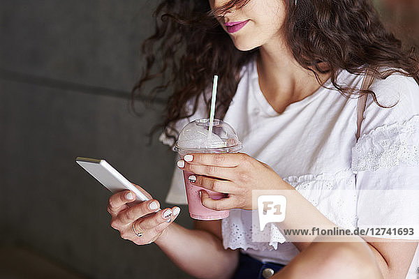 Woman's hands holding smartphone and plactic cup of smoothie