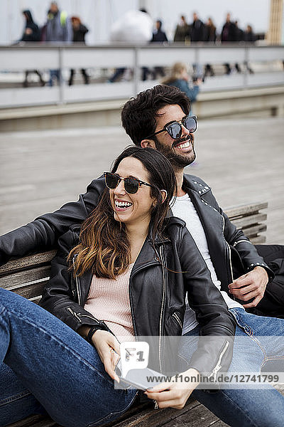 Spain  Barcelona  happy young couple with cell phone resting on a bench