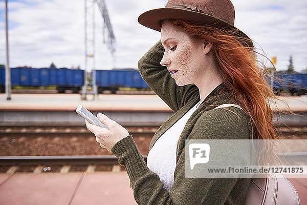Redheaded woman at platform looking at cell phone