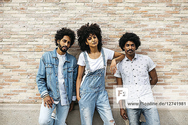 Portrait of three friends wearing denim standing in front of brick wall