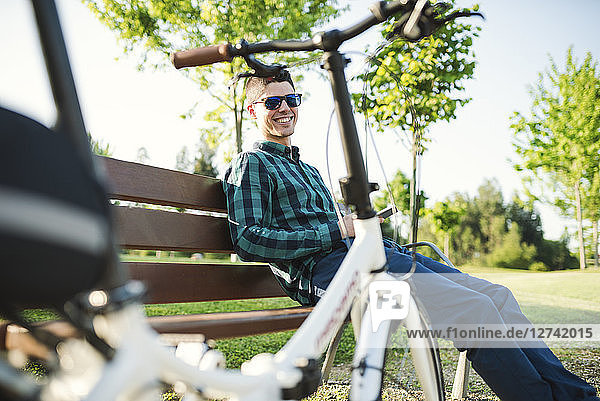 Smiling young man with smartphone on park bench