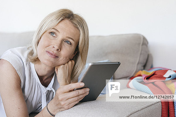 Portrait of mature woman lying on couch at home holding tablet
