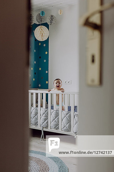 Baby boy standing in his cot  laughing