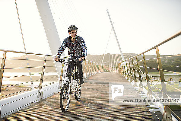 Young man riding bicycle on a bridge at sunset