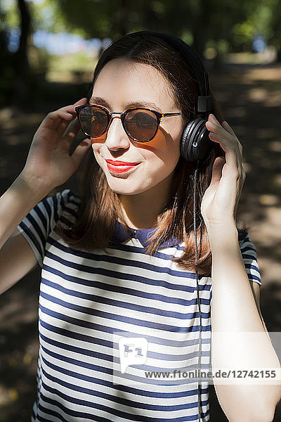 Portrait of smiling young woman wearing sunglasses listening music with headphones