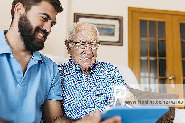 Adult grandson teaching his grandfather to use tablet