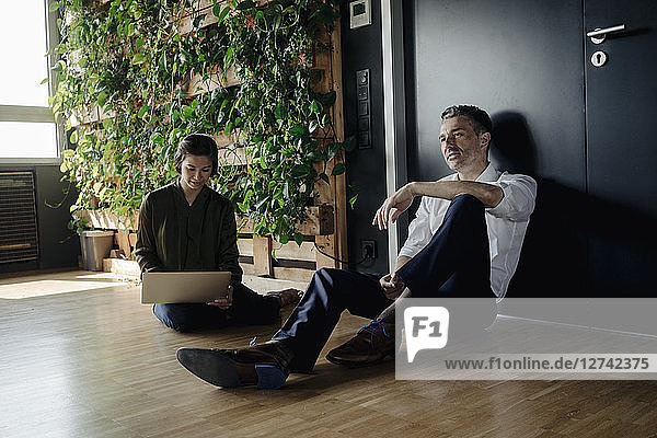 Businessman and businesswoman sitting on the floor in green office using tablet