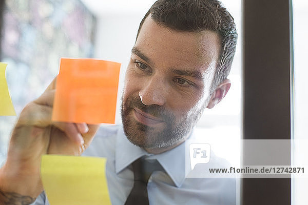 Businessman in office writing on adhesive note on glass wall