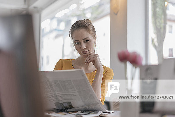 Young woman sitting in coworking space  reading newspaper