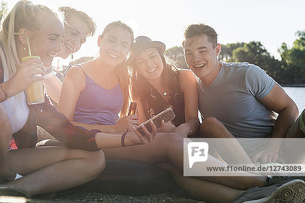Group of happy friends sitting outdoors with drinks and cell phone