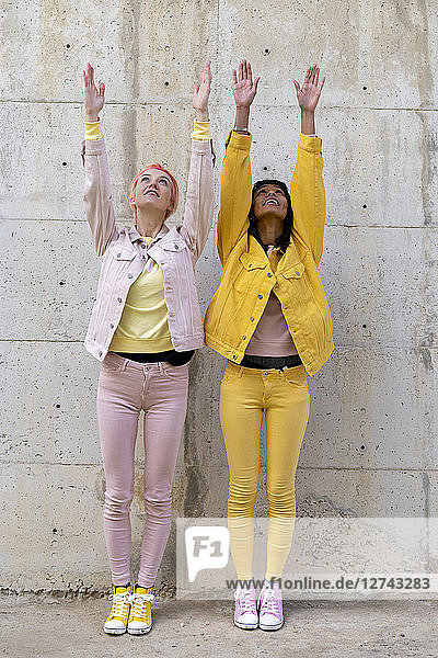Two alternative friends wearing yellow and pink jeans clothes  posing  raising arms