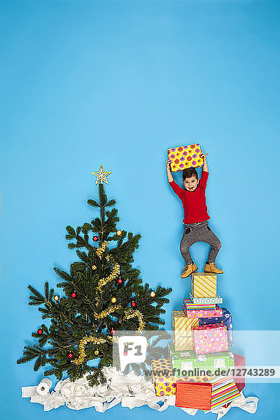 Boy standing on pile of Christmas presents next to Christmas tree