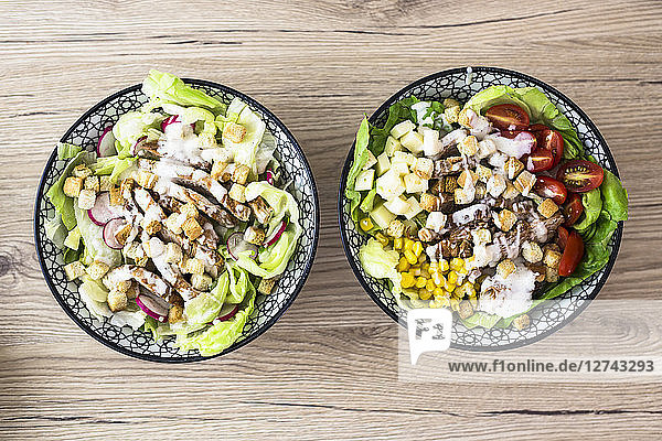 Two bowls of various Caesar salads with meat