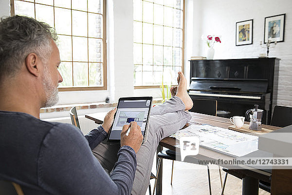 Mature man working from his home office with feet up  using tablet
