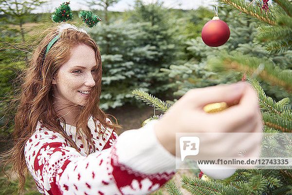 Redheaded young woman decorating Christmas tree outdoors