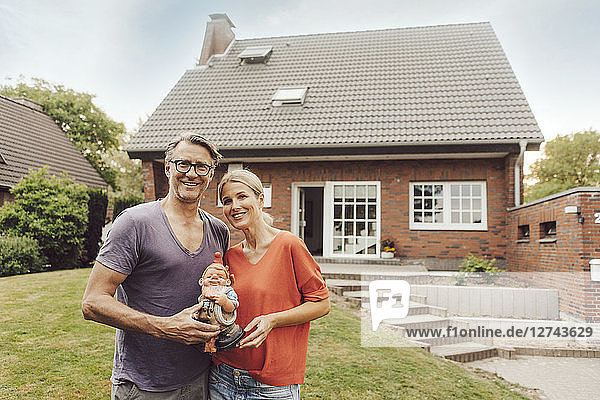 Portrait of smiling mature couple standing in front of their home holding garden gnome