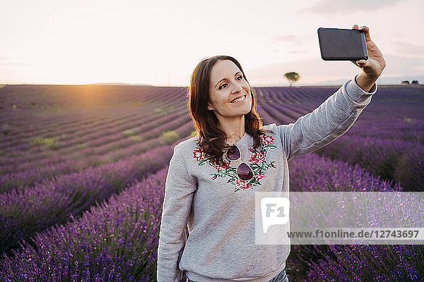 France  Valensole  portrait of smiling woman taking selfie in front of lavender field at sunset
