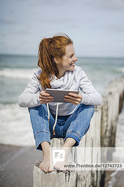 Woman sitting on fence at the beach using digital tablet at the sea