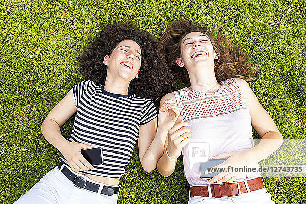 Two happy female friends lying down on grass and having fun
