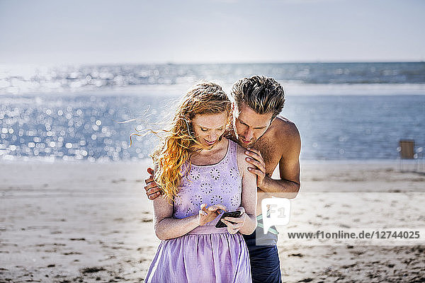 Netherlands  Zandvoort  couple on the beach looking at cell phone