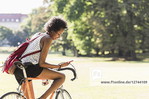 Young woman on bicycle in park checking cell phone