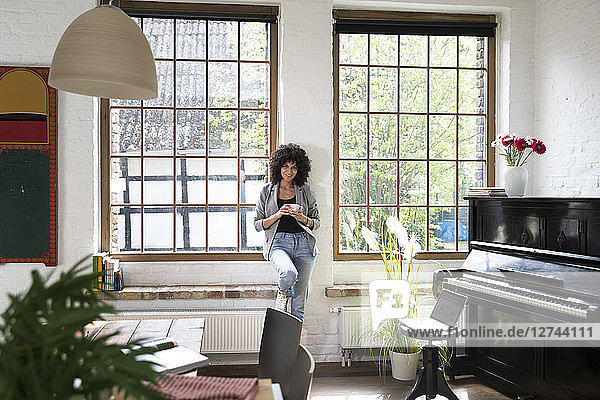 Woman standing at window of her loft apartment  drinking coffee
