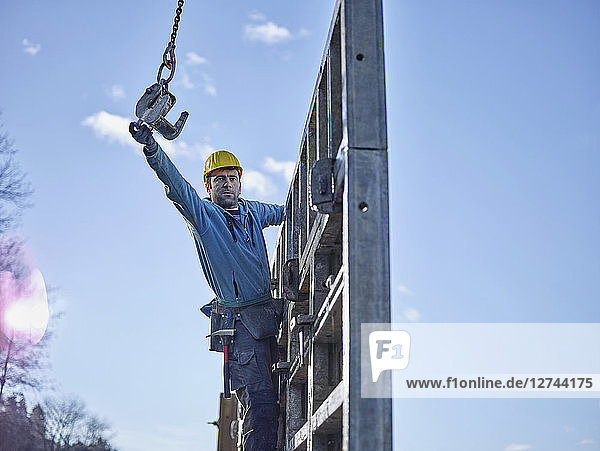 Construction worker reaching for hook of crane