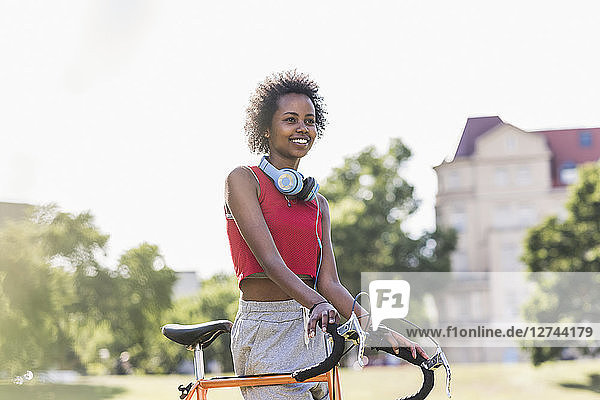 Smiling sporty young woman with bicycle in park