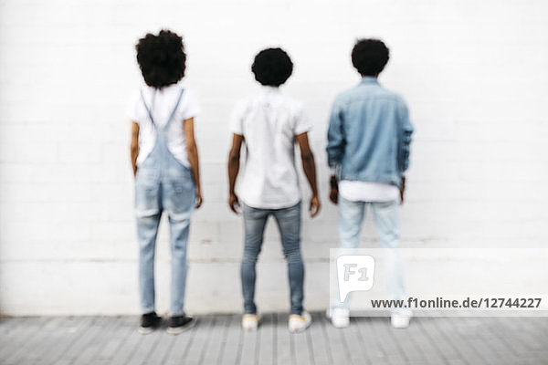 Back view of three friends standing side by side in front of white wall