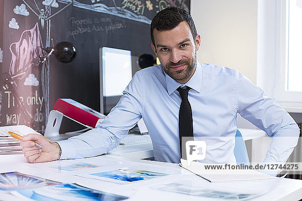 Portrait of confident businessman at desk in creative office