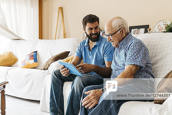 Adult grandson teaching his grandfather to use tablet