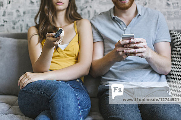Couple sitting on couch with remote control and smartphone  partial view