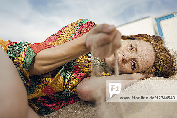 Redheaded woman lying on the beach  with sand trickling through her hand
