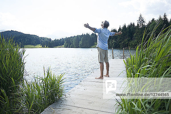 Germany  Mittenwald  mature man standing with arms outstretched on jetty at lake