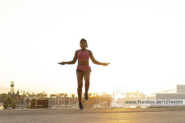 Spain  Barcelona  young black woman skipping rope at sunrise