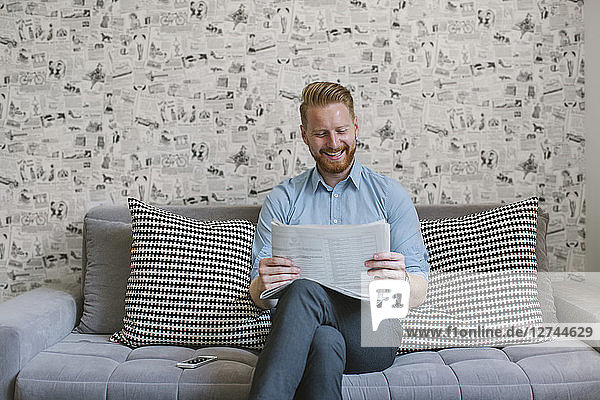 Smiling businessman reading newspaper on couch in his living room