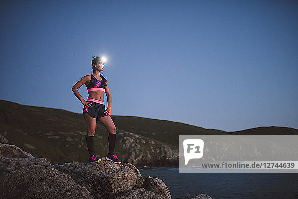 Sportive woman with headlamp standing on rocks in the evening