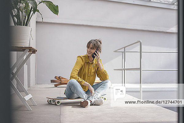 Young woman sitting on skateboard  using smartphone