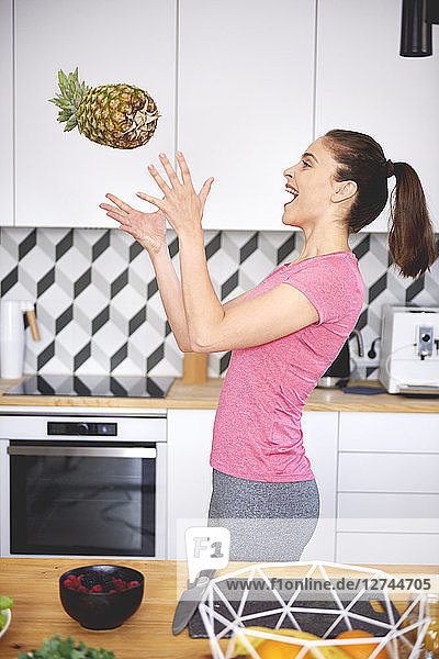 Young woman throwing pineapple in the air in the kitchen