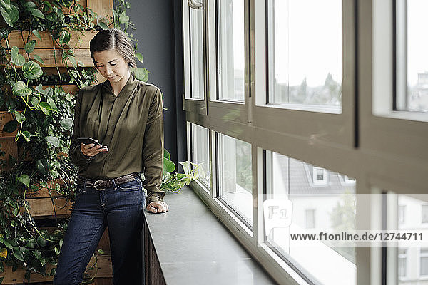 Young woman in office at the window looking at cell phone