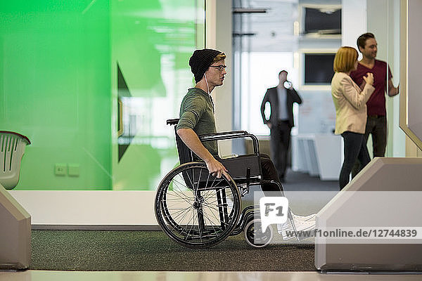 Young man in wheelchair listening to music in office