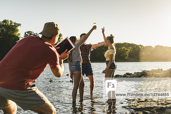 Group of happy friends with tablet in a river at sunset