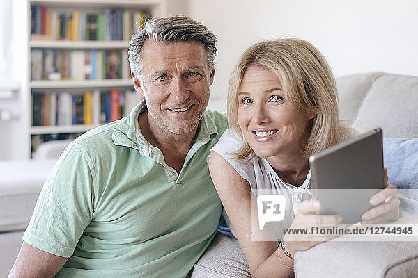 Portrait of smiling mature couple at home with tablet