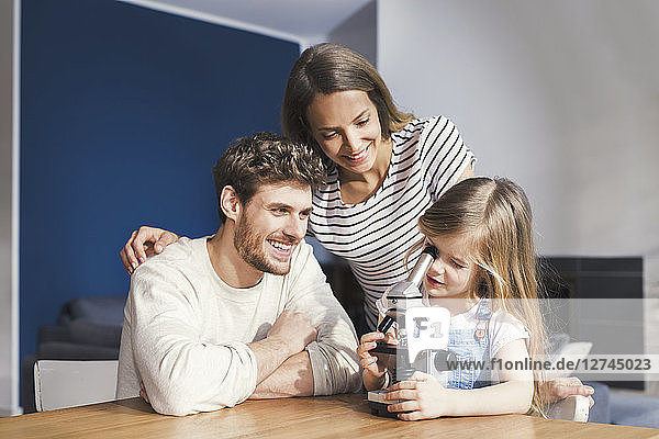 Parents watching daughter use a microscope  smiling proudly