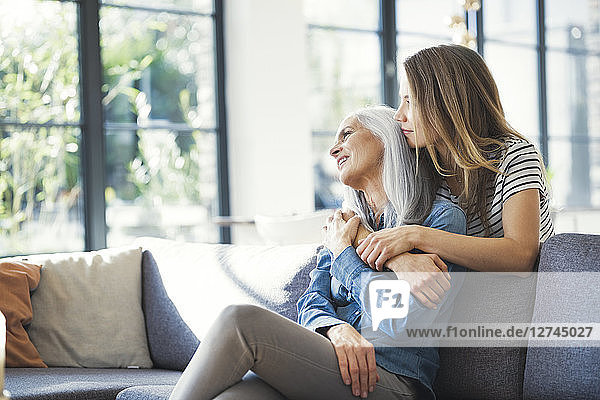 Daughter holding mother in her arms  sitting on couch